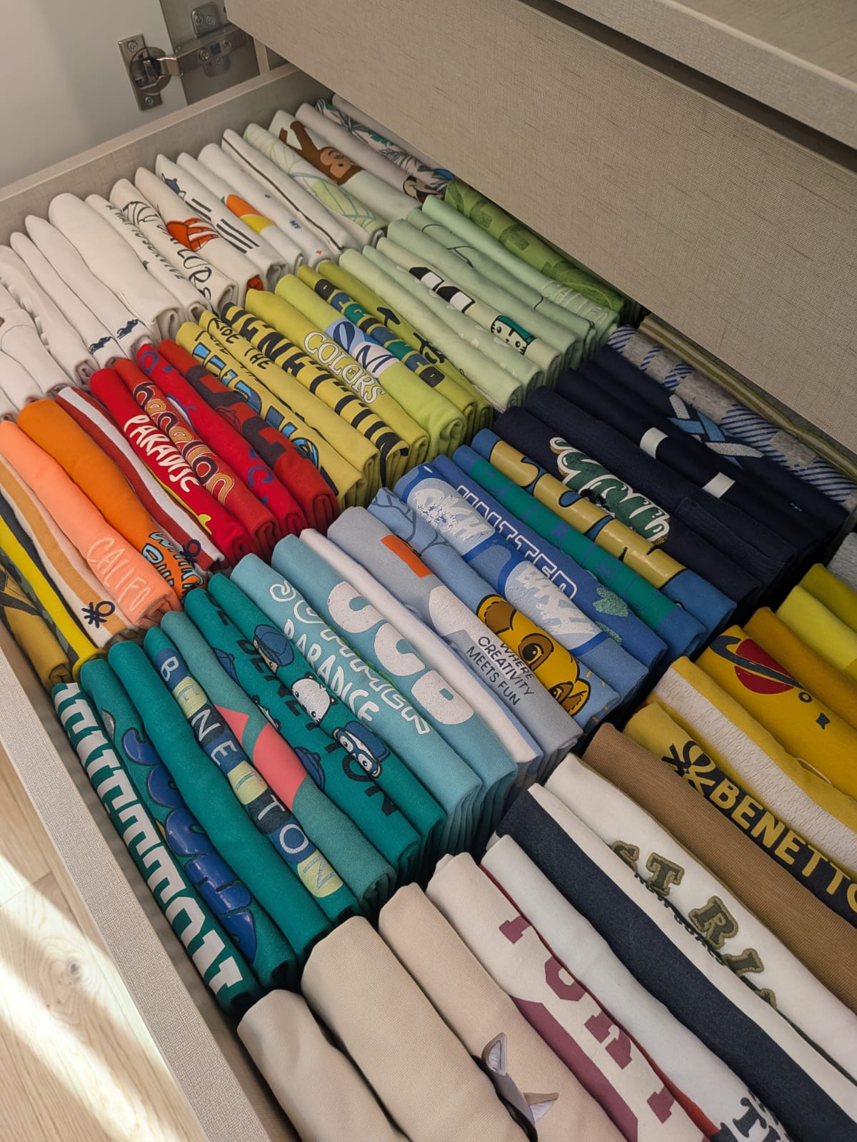 Gaveta com dezenas de t-shirts dobradas na vertical e organizadas por cor